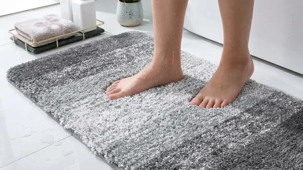 Wet feet stepping onto a grey and white ombre microfiber bath mat showing quick water absorption